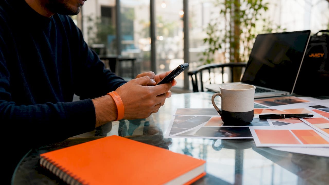 Hands typing on smartphone over cluttered desk